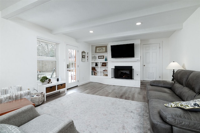 living room featuring a brick fireplace, beamed ceiling, hardwood / wood-style flooring, built in shelves, and radiator heating unit