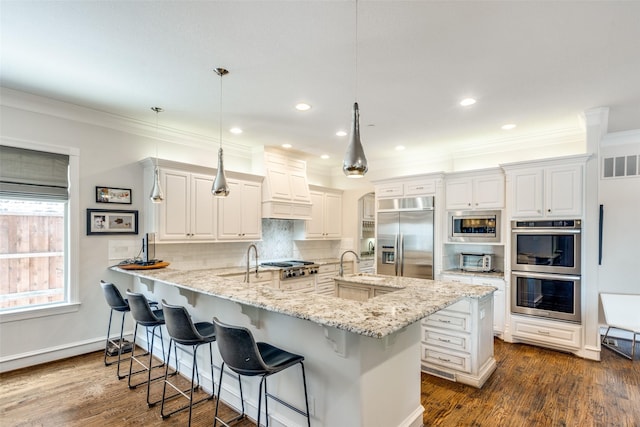 kitchen with a breakfast bar area, hanging light fixtures, light stone countertops, white cabinets, and built in appliances