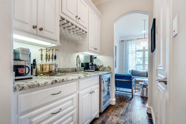 kitchen featuring light stone countertops, ornamental molding, white cabinets, dark hardwood / wood-style flooring, and beverage cooler