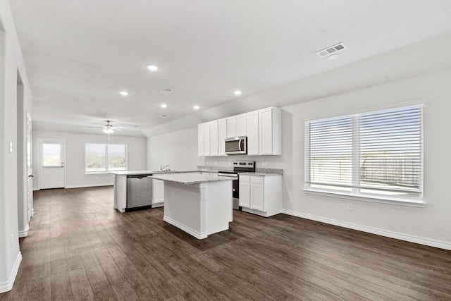 kitchen with white cabinets, appliances with stainless steel finishes, a kitchen island, dark hardwood / wood-style floors, and light stone counters