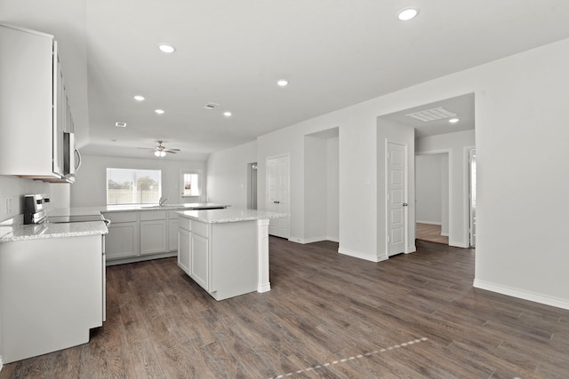 kitchen featuring dark wood-type flooring, stove, light stone countertops, white cabinets, and a center island