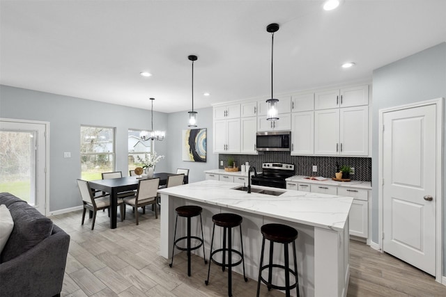 kitchen with pendant lighting, appliances with stainless steel finishes, white cabinetry, an island with sink, and light wood-type flooring