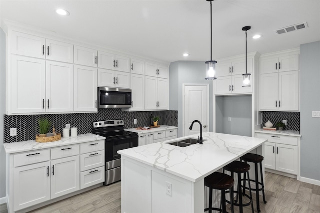 kitchen with white cabinets, appliances with stainless steel finishes, sink, and an island with sink