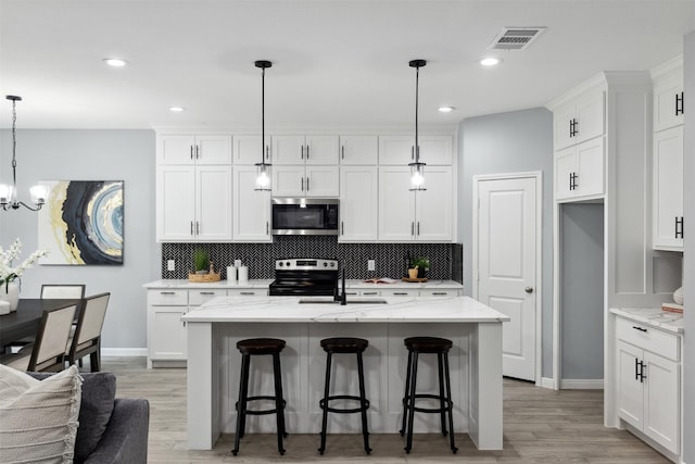 kitchen featuring stainless steel appliances, white cabinetry, pendant lighting, and an island with sink