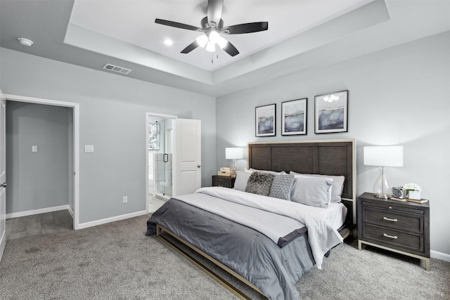 bedroom featuring ceiling fan, ensuite bathroom, carpet flooring, and a tray ceiling