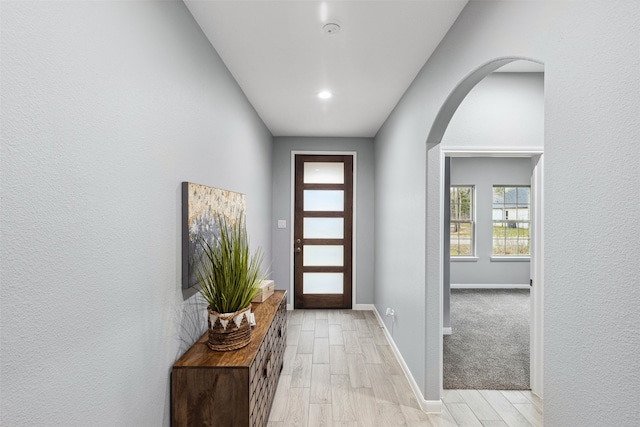 doorway with recessed lighting, arched walkways, baseboards, and light wood-type flooring