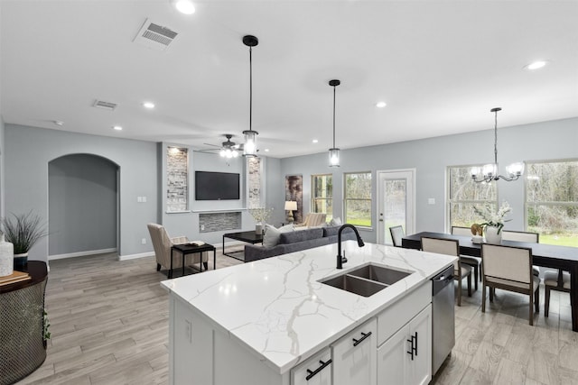 kitchen with dishwasher, hanging light fixtures, white cabinets, sink, and an island with sink