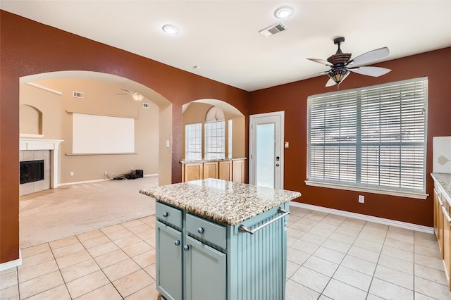 kitchen featuring light colored carpet, light stone countertops, a tile fireplace, and a center island