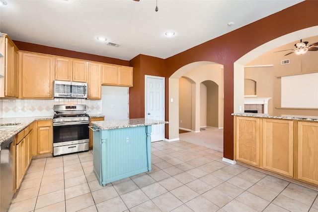 kitchen featuring ceiling fan, backsplash, light tile patterned flooring, light stone countertops, and appliances with stainless steel finishes