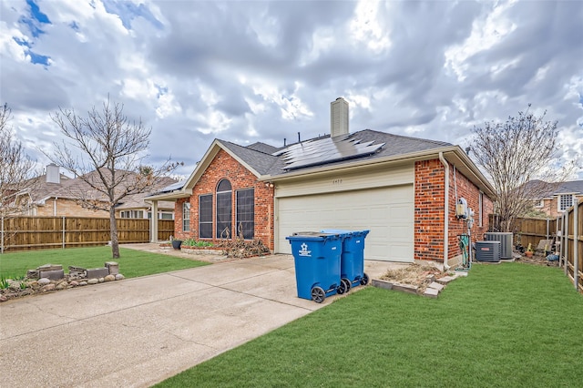 back of property with a garage, a yard, solar panels, and central air condition unit