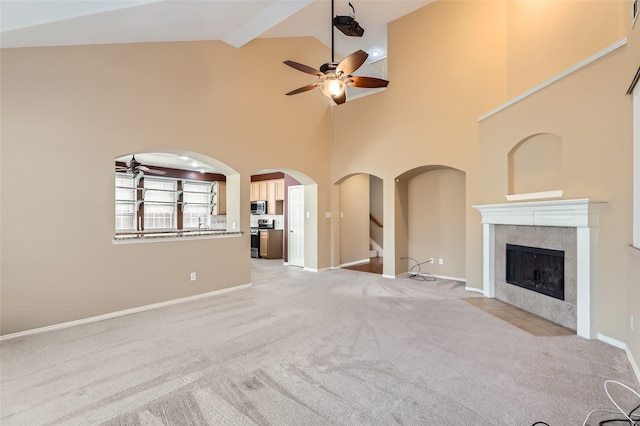 unfurnished living room with ceiling fan, light colored carpet, a tiled fireplace, and high vaulted ceiling