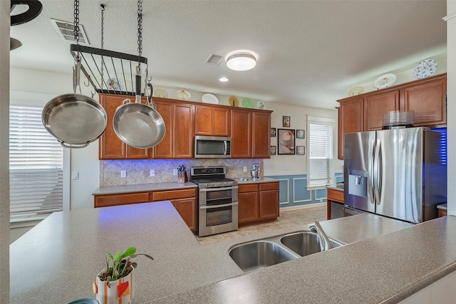 kitchen with stainless steel appliances, a sink, backsplash, a textured ceiling, and brown cabinetry