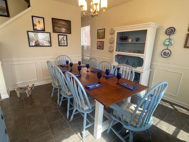 dining room featuring a chandelier, a decorative wall, and wainscoting