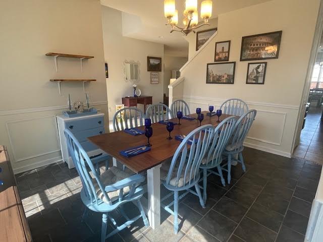 dining room with wainscoting, a chandelier, stairway, and a decorative wall