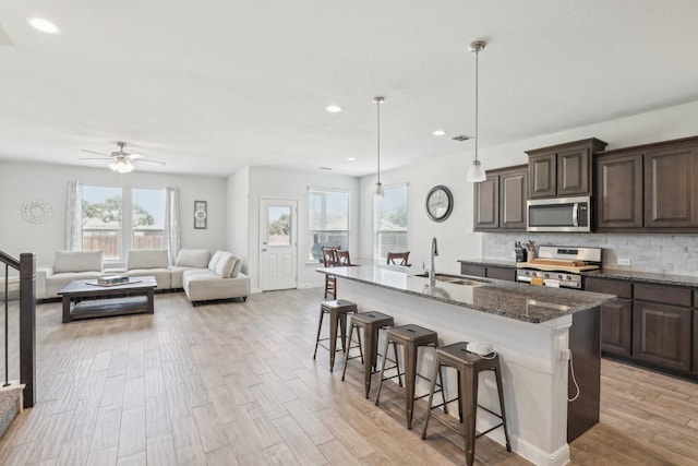 kitchen featuring sink, an island with sink, appliances with stainless steel finishes, and dark stone countertops