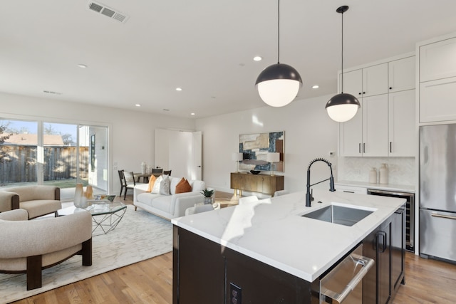 kitchen with pendant lighting, white cabinetry, stainless steel appliances, an island with sink, and sink