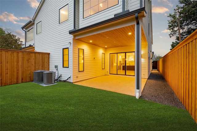 back house at dusk featuring a lawn, central AC, and a patio area