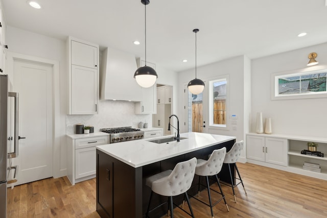 kitchen with pendant lighting, sink, an island with sink, custom range hood, and white cabinets