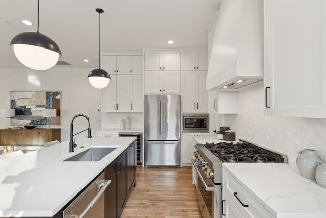 kitchen featuring premium range hood, white cabinetry, appliances with stainless steel finishes, decorative light fixtures, and sink