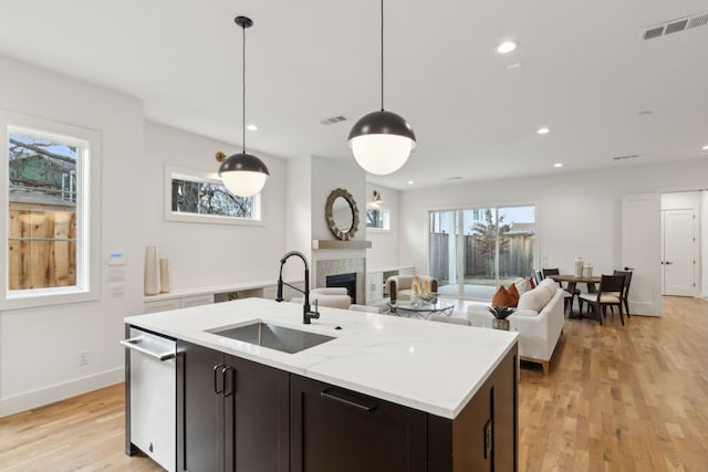 kitchen featuring a tiled fireplace, light stone countertops, pendant lighting, light hardwood / wood-style flooring, and sink