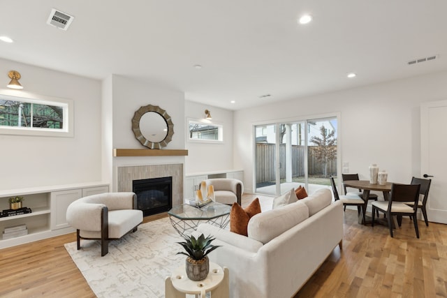 living room with built in features, a fireplace, and light hardwood / wood-style floors