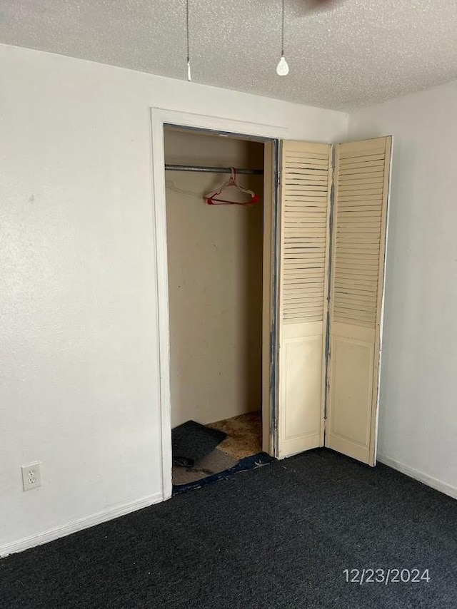 unfurnished bedroom with a textured ceiling, a closet, and dark colored carpet