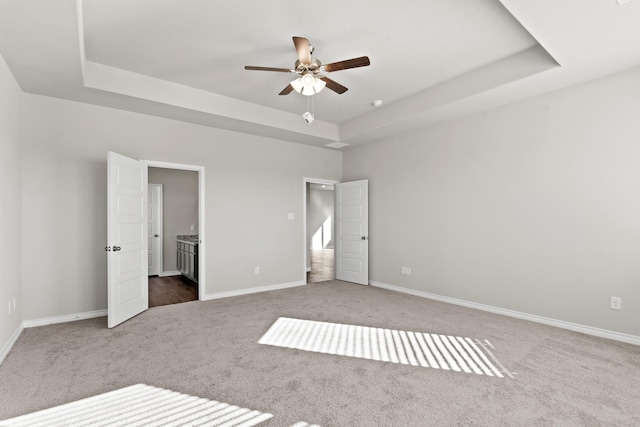 unfurnished bedroom with carpet, connected bathroom, a tray ceiling, and baseboards