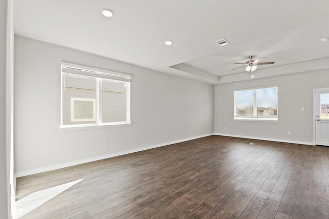 spare room featuring a ceiling fan, visible vents, baseboards, dark wood-style floors, and a raised ceiling