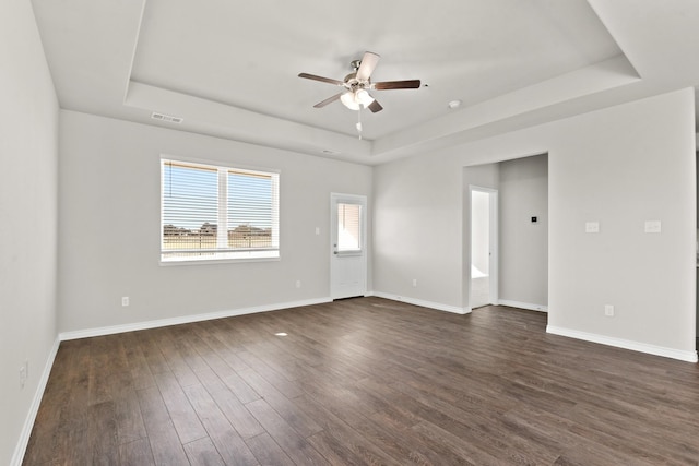 spare room with baseboards, visible vents, a tray ceiling, and dark wood-style flooring