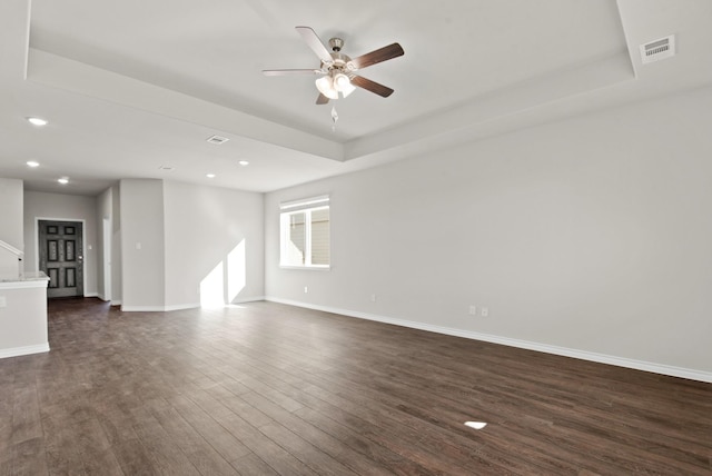 empty room with dark wood-style floors, a tray ceiling, visible vents, a ceiling fan, and baseboards