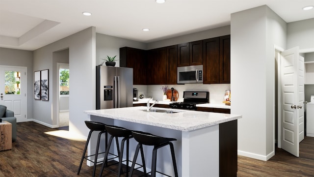 kitchen with appliances with stainless steel finishes, a kitchen island with sink, sink, dark brown cabinets, and dark hardwood / wood-style flooring