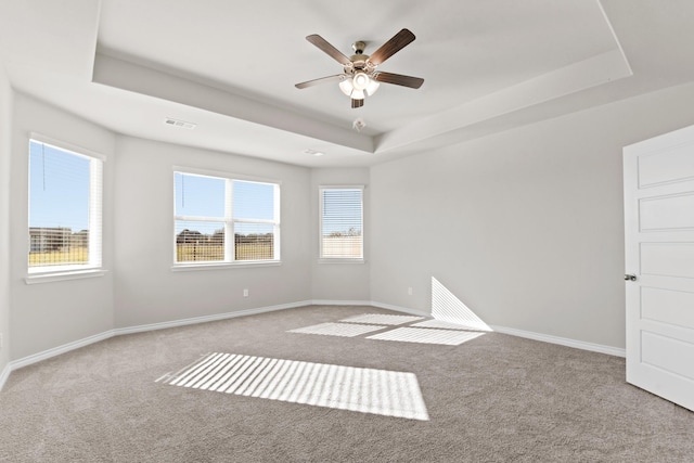 empty room with carpet floors, plenty of natural light, a raised ceiling, and visible vents