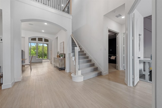 entryway featuring visible vents, arched walkways, a towering ceiling, stairway, and wood finished floors