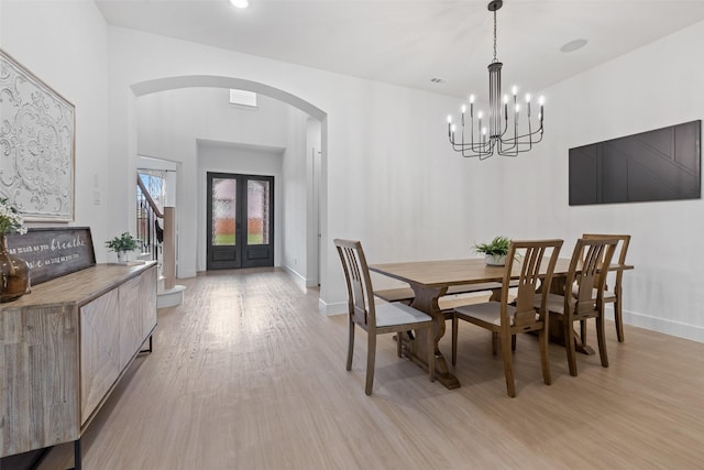 dining area with arched walkways, french doors, light wood-style floors, baseboards, and stairs