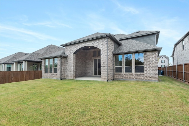 back of house with a fenced backyard, roof with shingles, a yard, a patio area, and brick siding