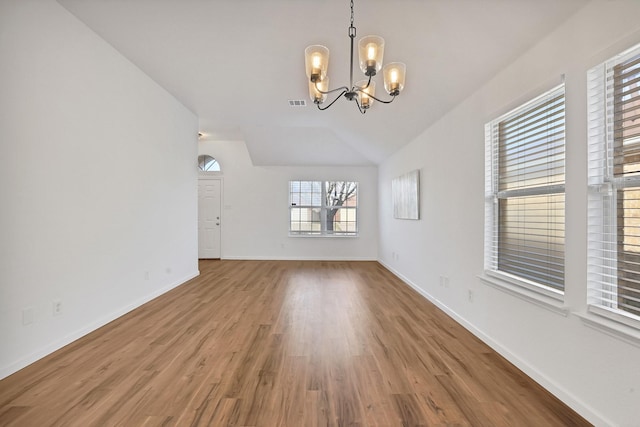 unfurnished living room featuring lofted ceiling, hardwood / wood-style flooring, and a notable chandelier