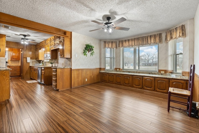 kitchen featuring ceiling fan, dishwasher, wood walls, hardwood / wood-style floors, and a textured ceiling