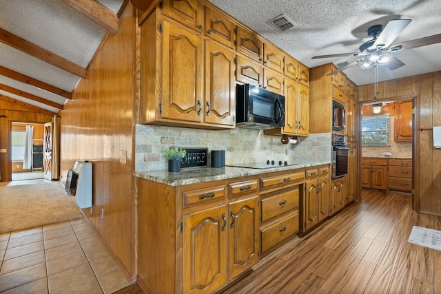 kitchen featuring ceiling fan, black appliances, lofted ceiling with beams, heating unit, and light stone countertops