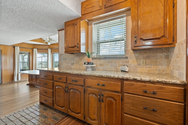 kitchen with ceiling fan, decorative backsplash, dark hardwood / wood-style floors, light stone countertops, and a textured ceiling