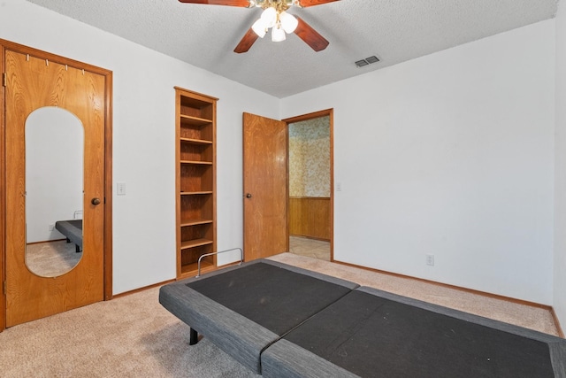 exercise area featuring a textured ceiling, ceiling fan, and light colored carpet