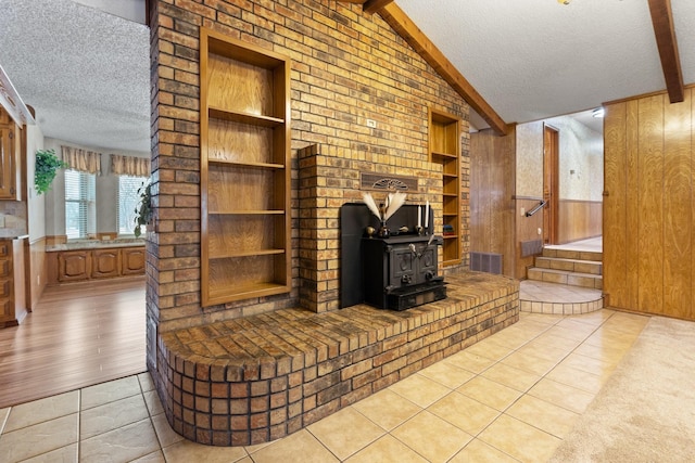 tiled living room with a textured ceiling, a wood stove, wooden walls, and lofted ceiling with beams