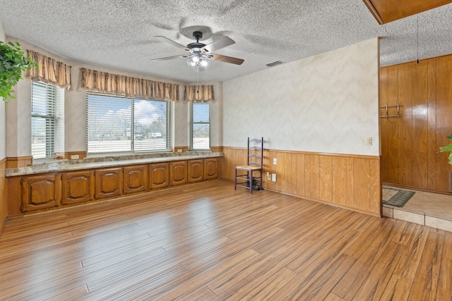 kitchen with wood walls, ceiling fan, a textured ceiling, and light hardwood / wood-style flooring