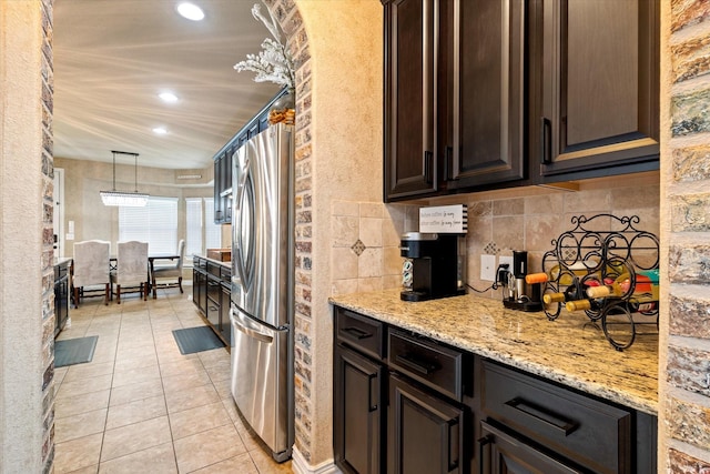 kitchen with light tile patterned floors, dark brown cabinetry, pendant lighting, light stone counters, and stainless steel fridge