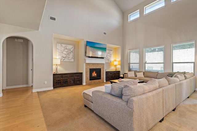 living room featuring light wood-type flooring, a towering ceiling, and a fireplace