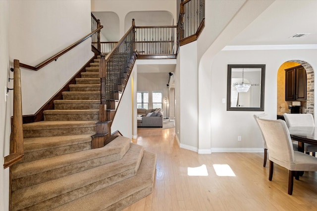 stairs with hardwood / wood-style flooring, a high ceiling, crown molding, and a chandelier