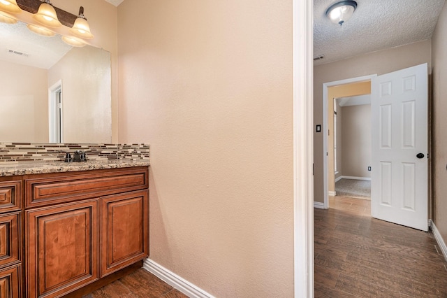 bathroom featuring vanity, wood-type flooring, backsplash, and a textured ceiling