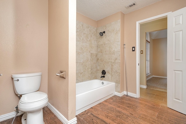 bathroom with wood-type flooring, toilet, tiled shower / bath combo, and a textured ceiling