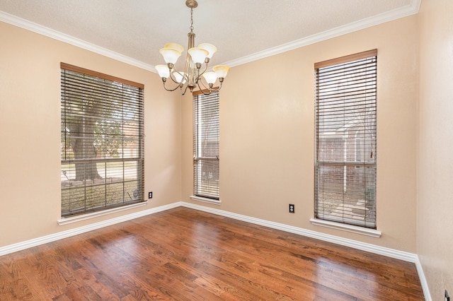 spare room featuring a notable chandelier, crown molding, a wealth of natural light, and hardwood / wood-style flooring