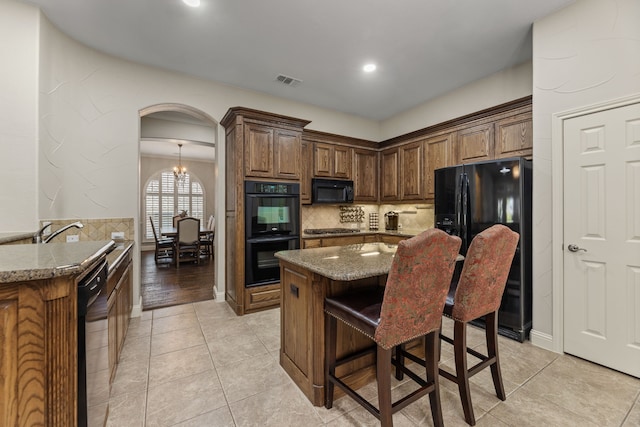 kitchen with black appliances, light stone countertops, decorative backsplash, an inviting chandelier, and a breakfast bar