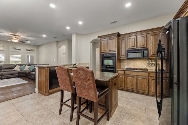 kitchen featuring black appliances, a kitchen island, light tile patterned flooring, and backsplash